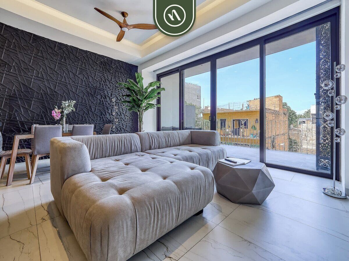 Una sala de estar moderna con un sofá modular grande, un comedor con mesa y sillas, y un ventanal con vistas a la ciudad.
