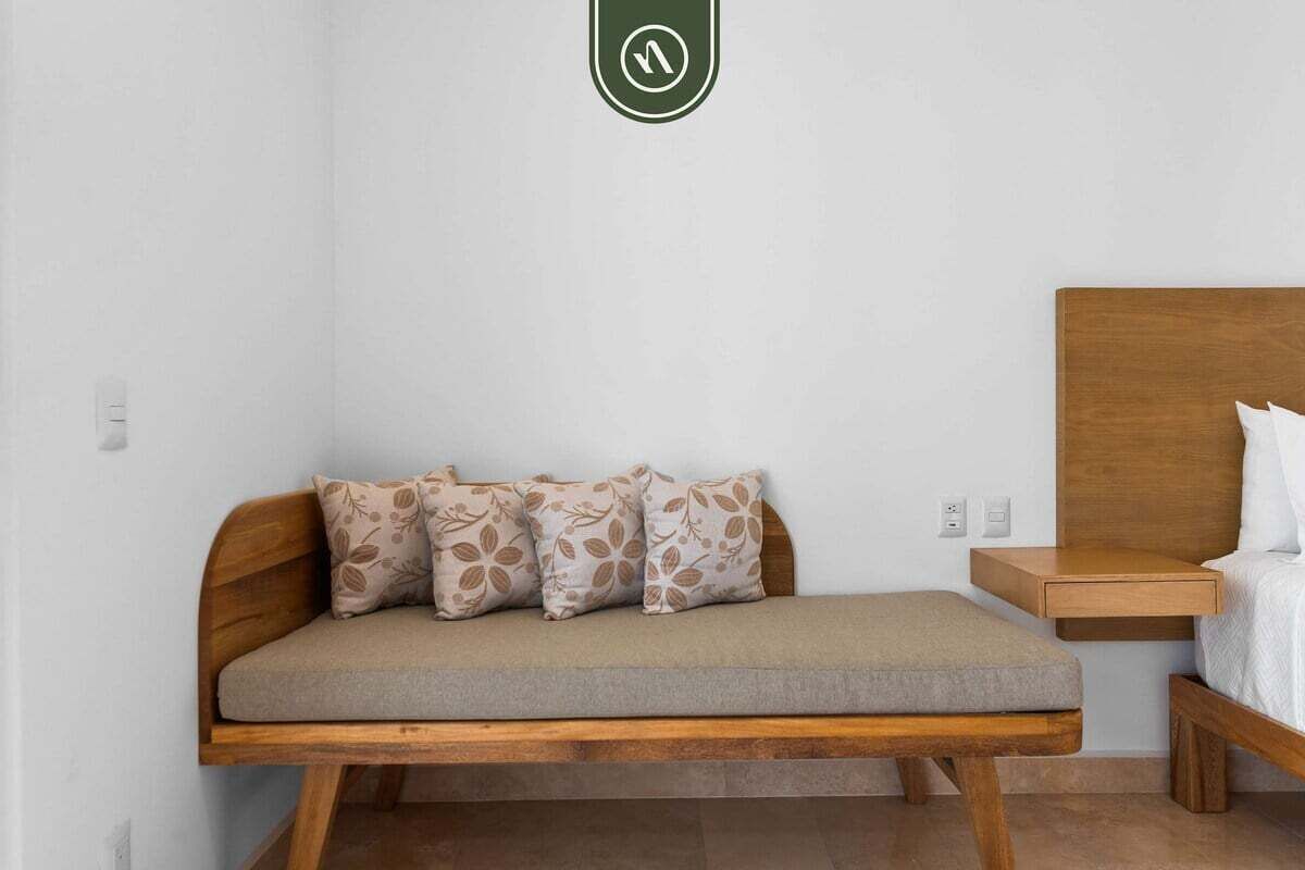 A room with a wooden bench, a bed with a wooden headboard, and a small wooden nightstand.