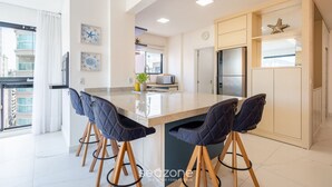 Una cocina moderna con una isla central, taburetes de bar y vista al balcón.