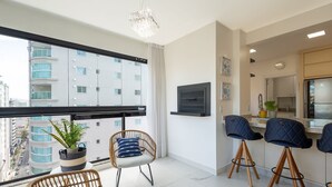 Un apartamento moderno con balcón, sillas de mimbre, una planta en maceta y una zona de cocina con taburetes de bar.