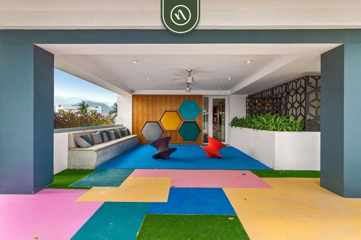 Un espacio interior moderno con un diseño geométrico en el suelo, una zona de estar con cojines y una pared con patrones hexagonales.