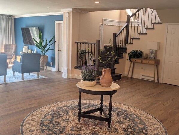 A living room with a round table, a staircase, and a blue wall. - Private Waterfront Paradise |Heated Pool, Sauna, HotTub, Pontoon Boat, Billiard (Beaverton)