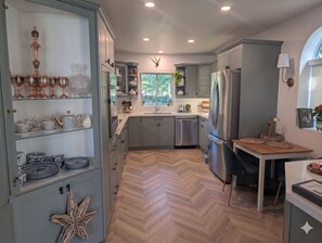 A modern kitchen with grey cabinets, stainless steel appliances, and a herringbone wood floor.