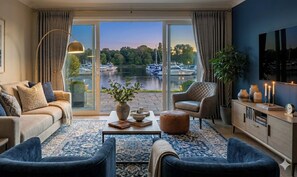 A living room with a sofa, armchair, and ottoman, a coffee table, a sideboard, and a view of boats on a lake through large glass doors. - Private Waterfront Paradise |Heated Pool, Sauna, HotTub, Pontoon Boat, Billiard (Beaverton)