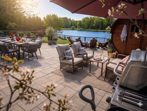 An outdoor patio with a grill, seating, and a view of a lake. - Private Waterfront Paradise- Pool, Sauna, Hot Tub, Pontoon Boat, Billiard, Bikes (Beaverton)
