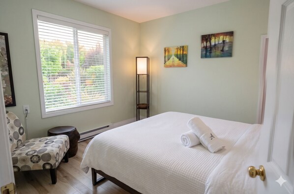 A bedroom with a bed, a chair, a floor lamp, and a painting on the wall.
