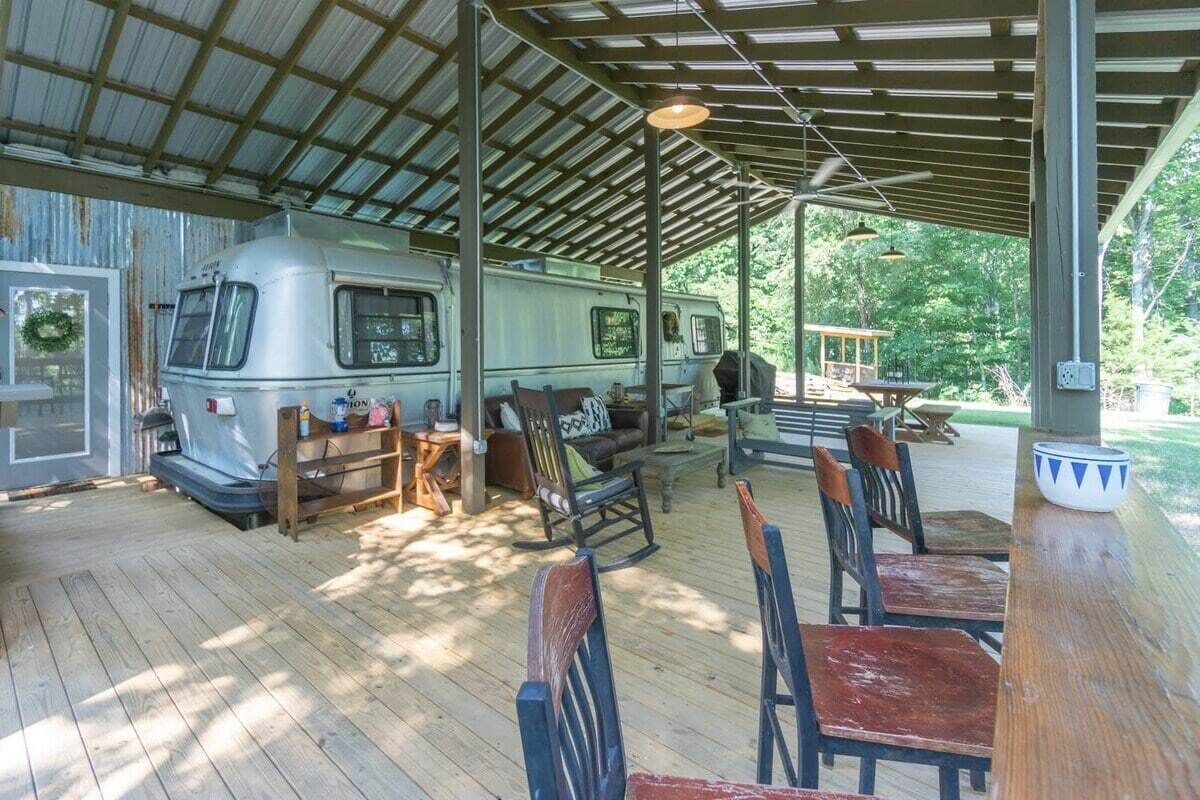 Een overdekt buitengebied met een camper en houten meubilair.