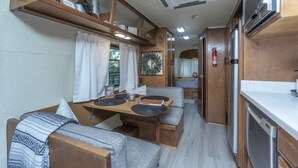 Interior d'una caravana compacta, amb zona de dinar, cuina americana i un petit espai d'estar.