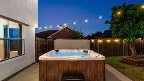 A hot tub in a backyard with a wooden fence, string lights, and a house in the background. - NEW Villa w/ Pool•HotTub•GameRoom•Movie•Sleeps20 (Austin)