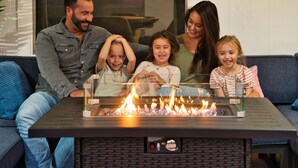 Una familia sentada en un sofá frente a una chimenea con una mesa de vidrio.