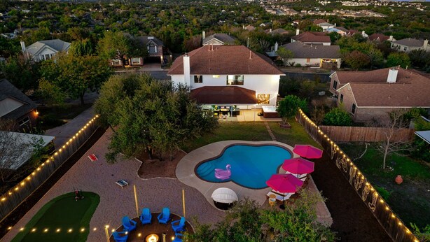 Un patio trasero residencial con piscina, mobiliario exterior y un hogar para fogata.