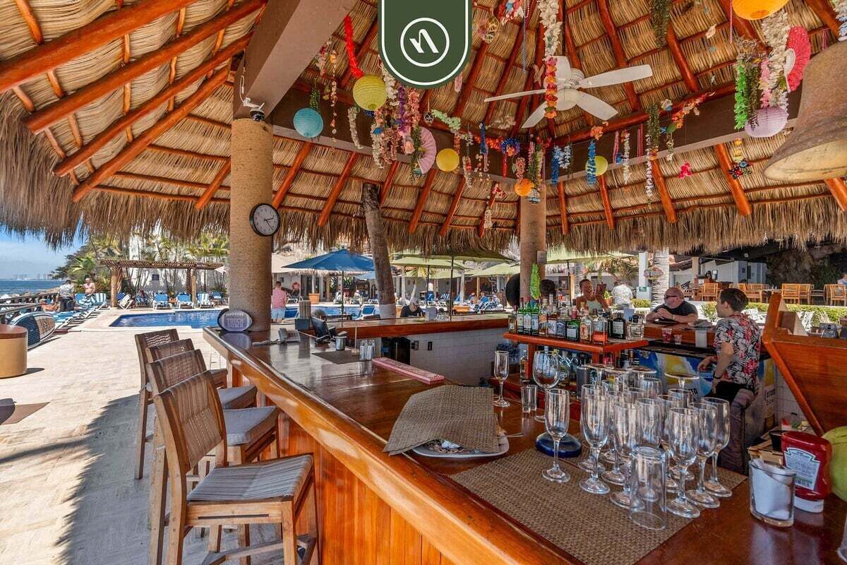 Un bar situé en bord de mer, doté d’un toit de chaume, de tables en plein air et offrant une vue sur l’océan.