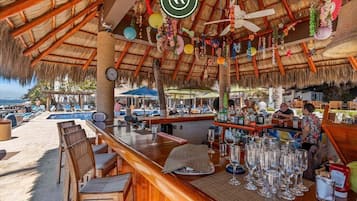 Un bar situé en bord de mer, doté d’un toit de chaume, de tables en plein air et offrant une vue sur l’océan.