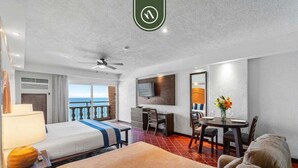 Habitación de hotel con cama, escritorio, silla, televisor y balcón con vistas.