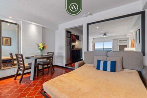 Ein Hotelzimmer mit Bett, Esstisch mit Stühlen, Küchenzeile und Blick ins Freie.