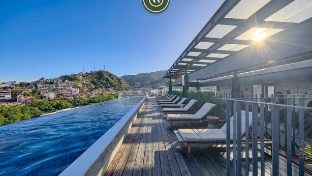 Terraza de madera con piscina y sillas reclinables con vistas a un paisaje urbano.