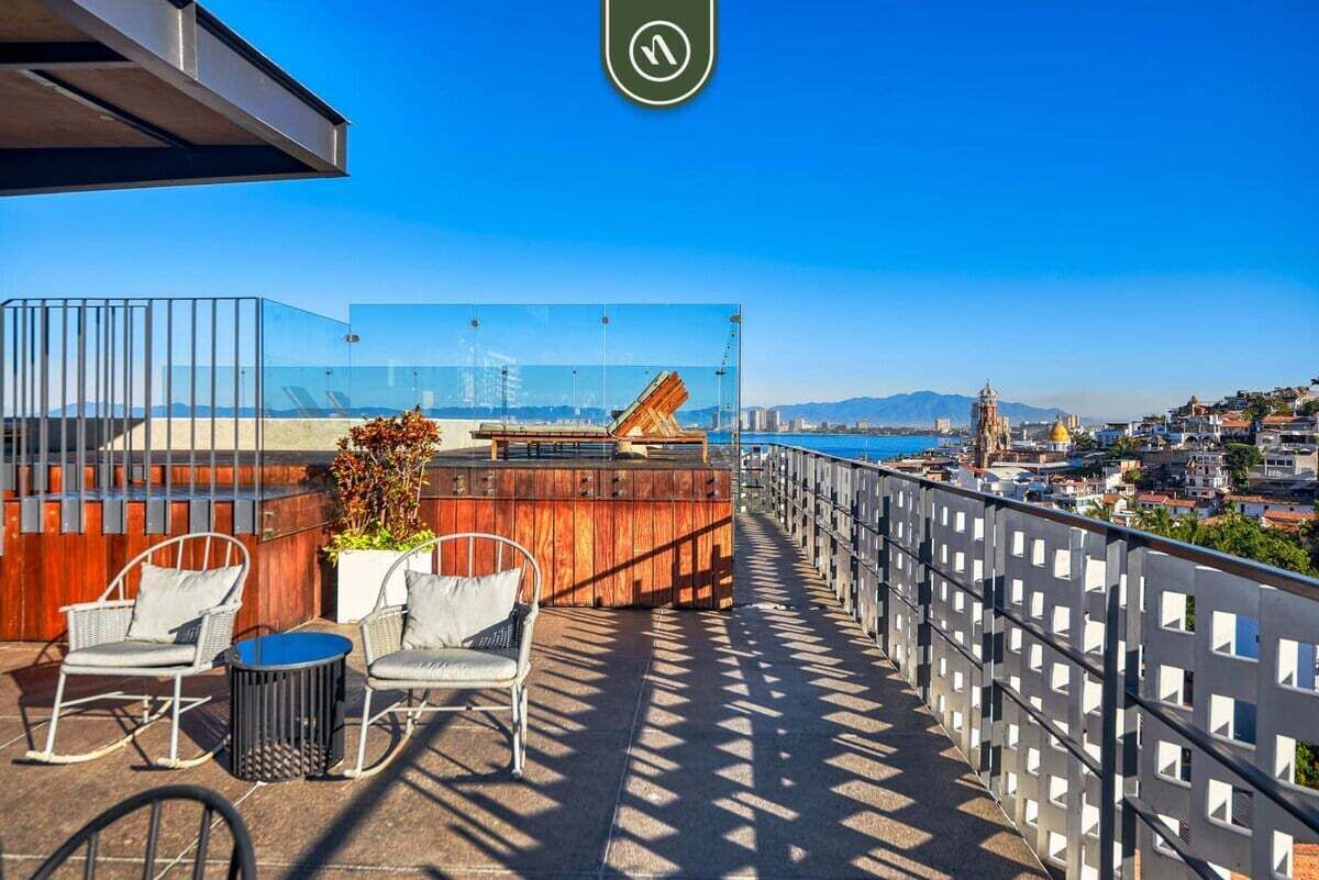 A balcony with outdoor seating, a view of the city, and a clear sky.