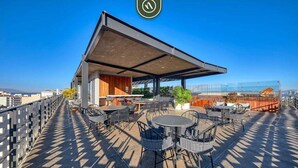 Una terraza en la azotea con mobiliario exterior, una zona cubierta y vistas panorámicas de la ciudad.