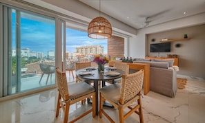 A modern living room with a dining area, large windows, and a city view.