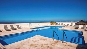 Una piscina en la azotea con agua cristalina, rodeada de sillones de descanso y vistas al océano.