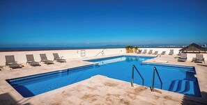 A rooftop pool with clear blue water, surrounded by lounge chairs and a view of the ocean.