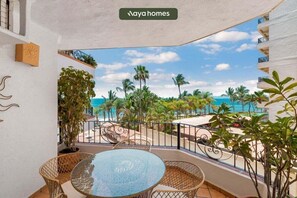 A balcony with a glass table and chairs, overlooking a beach with palm trees and a clear sky. - Puerto Vallarta 2BR/2BA Condo Near Beach, Pool & WiFi (Puerto Vallarta)