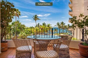 A balcony with a round table and wicker chairs, overlooking a pool and palm trees. - Puerto Vallarta 2BR/2BA Condo Near Beach, Pool & WiFi (Puerto Vallarta)