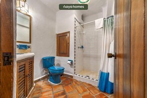 A bathroom with a shower, two toilets, a wooden door, and a tiled floor.