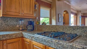 Une cuisine dotée de plans de travail en granit, d’armoires en bois, d’une cuisinière à gaz et d’une machine à café.