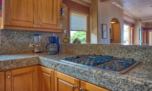 Una cocina con encimeras de granito, armarios de madera, estufa a gas y cafetera.