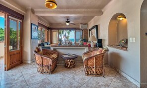 A room with wicker furniture, a ceiling fan, and a view to the outside.