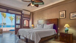 Une chambre à coucher avec un lit, des lampes de chevet, une table de nuit, un ventilateur de plafond et une vue sur des palmiers et une plage.