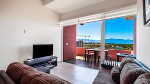 A living room with a flat-screen TV, two sofas, a coffee table, and a balcony with a chessboard.