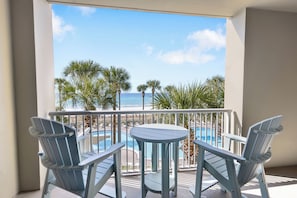Un balcon avec deux chaises et une table, donnant sur une piscine et des palmiers.