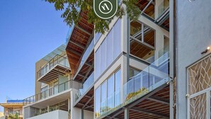 Um edifício moderno de vários andares, com varandas, janelas amplas e uma unidade de ar condicionado visível.