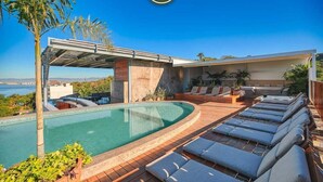 Uma área de piscina com espreguiçadeiras, um espaço de estar coberto e vista para o mar.