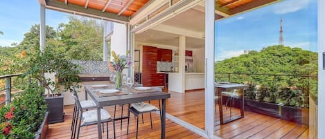 A spacious outdoor deck with a dining area, a kitchen, and a view of a tower.