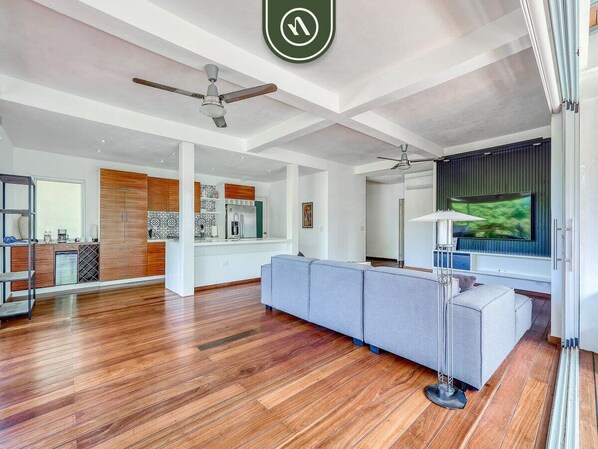 A spacious living area with a large grey sofa, wooden flooring, ceiling fans, and a television. - The Ava Unit 16 | 2BR/3BA Puerto Vallarta, pool, gym, hot tub (Puerto Vallarta)
