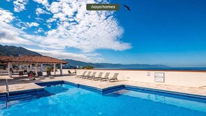 A pool area with lounge chairs, a covered seating area, and a view of the sea and mountains. - 303-VistadelSol | 2BR/2BA Puerto Vallarta, Ocean View (Puerto Vallarta)