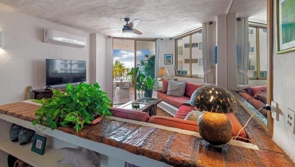 A living room with a TV, sofa, coffee table, and plants. - 303-VistadelSol | 2BR/2BA Puerto Vallarta, Ocean View (Puerto Vallarta)