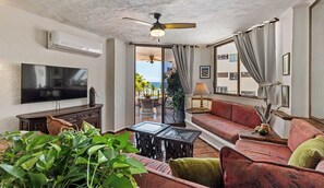 A living room with a TV, sofa, and a balcony with a view of the ocean. - 303-VistadelSol | 2BR/2BA Puerto Vallarta, Ocean View (Puerto Vallarta)