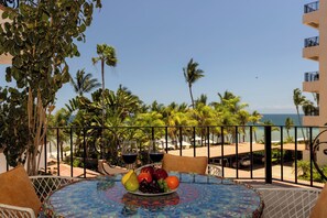 Une table avec une assiette de fruits, deux verres à vin et une vue sur la plage et l’océan.