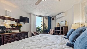 A bedroom with a large bed, a TV, a dresser, and a window with a view. - 303-VistadelSol | 2BR/2BA Puerto Vallarta, Ocean View (Puerto Vallarta)