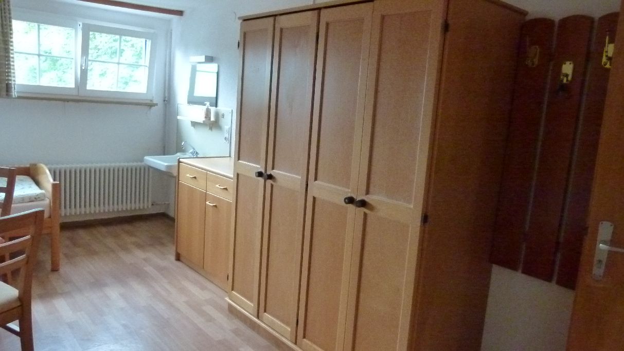 Een kamer met een houten kast, een radiator, een wastafel en een raam.