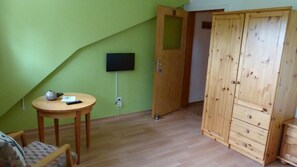 Een kamer met een groene muur, een houten garderobe, een klein rond tafeltje met een vaas en afstandsbediening, en een aan de muur bevestigde televisie.