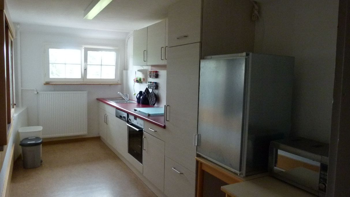 Una cocina con refrigerador, microondas, horno y ventana con persianas.
