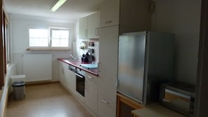 A kitchen with a refrigerator, microwave, oven, and a window with blinds.