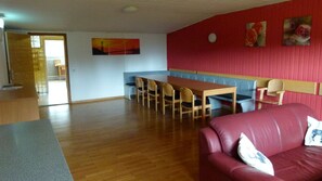 Een kamer met een houten eettafel, stoelen, een rode leren bank en een bankje.