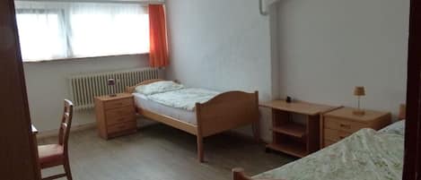 Un dormitorio con una cama individual, un escritorio, una silla y un radiador.