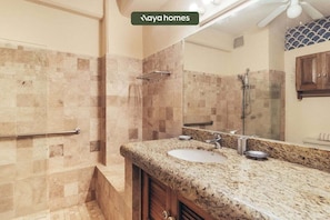 A bathroom with a granite countertop, a sink, a mirror, and a shower area.